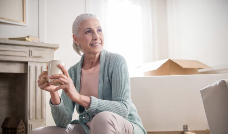 portrait of smiling woman drinking coffee and looking away at home